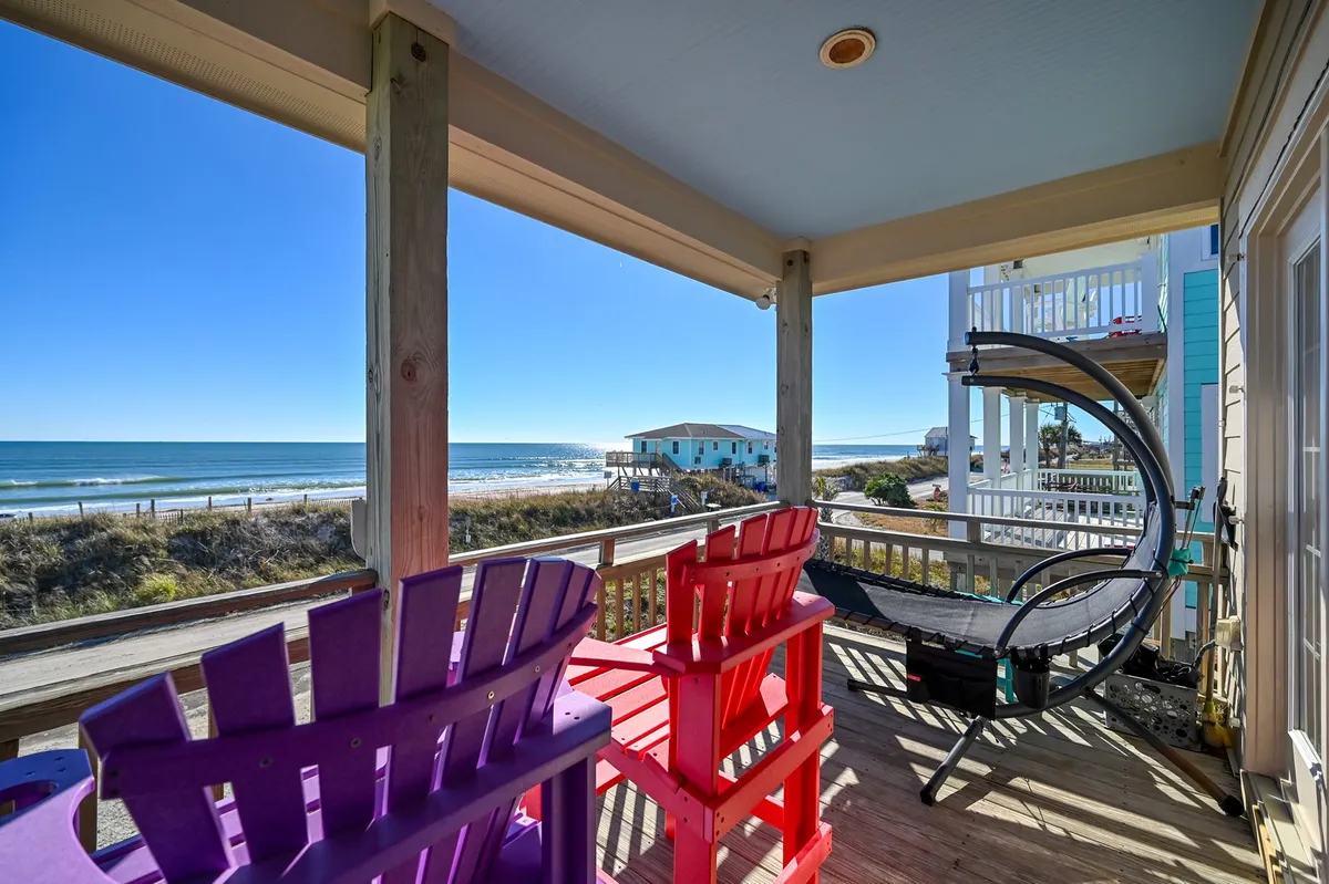 A welcoming porch scene with colorful chairs arranged to face an expansive ocean view, complemented by a hammock that invites relaxation. The bright exterior setting and ample seating evoke the perfect spot for couples to enjoy tranquil moments together, from morning coffee to sunset reflections.