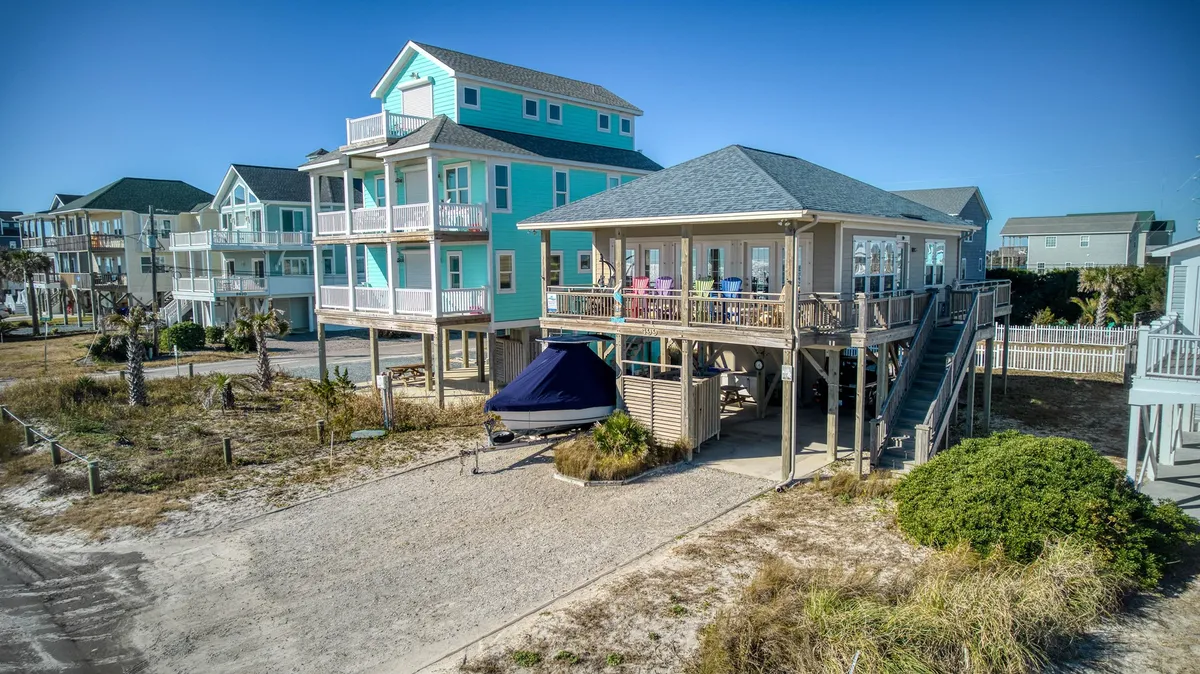 This exterior image features the elevated beach house with a boat parked beneath, highlighting the covered area that could serve as sheltered parking. The vibrant color of the house adds to the cheerful, welcoming mood, and the visible deck hints at easy access for unloading after a day at the beach.