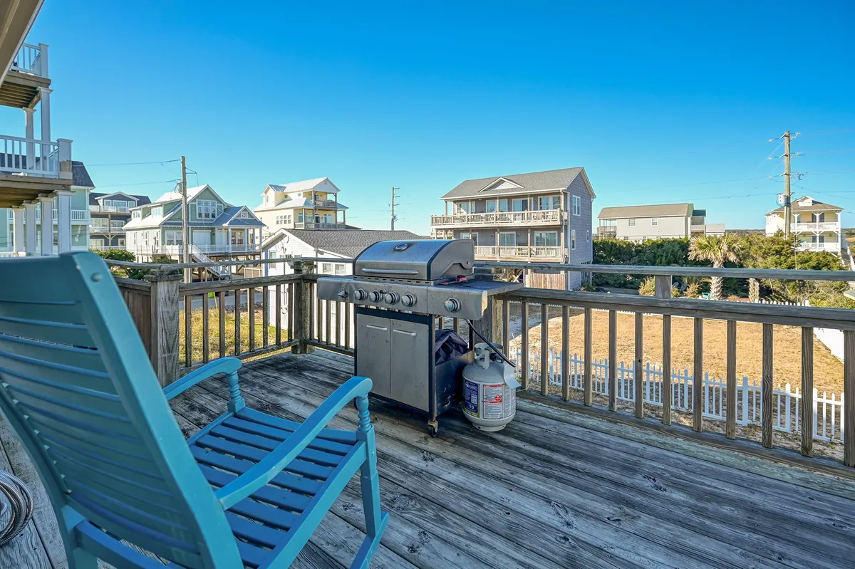 An inviting outdoor deck scene featuring a grill, blue chair, and sturdy deck railing. The space is positioned for enjoying fresh air, sunset views, and social barbecues, bridging the cottage with the surrounding beach environment.