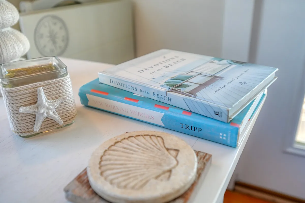 A tranquil reading nook featuring a decorative shell, thoughtfully arranged books, and a softly glowing candle. The intimate setup encourages peaceful reflection, reading, or meditation, reinforcing the cottage’s retreat-like ambiance.
