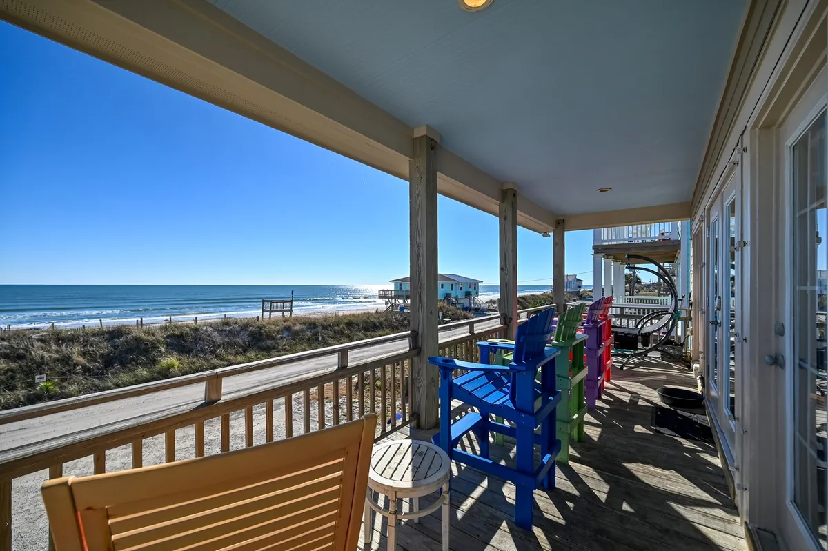 An oceanfront porch scene with colorful Adirondack chairs set on a wooden deck, overlooking expansive water views. The inviting setup encourages outdoor relaxation, sunrise coffees, or socializing with friends and family in a breathtaking coastal setting.