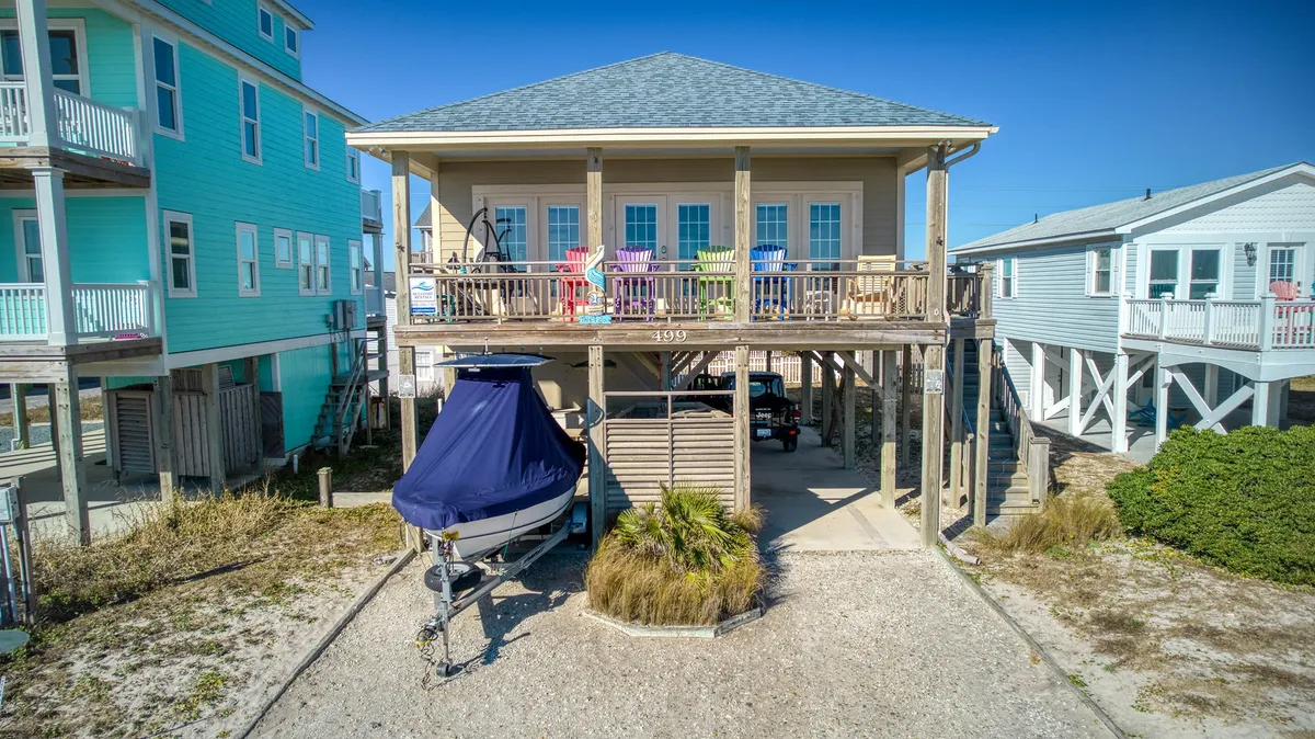 An exterior view of the vintage cottage with a spacious deck adorned with colorful chairs and a boat nearby. The open setting provides a direct connection to the ocean and hints at the relaxed beach lifestyle, with ample space for savoring the sea breeze or unwinding at sunset.