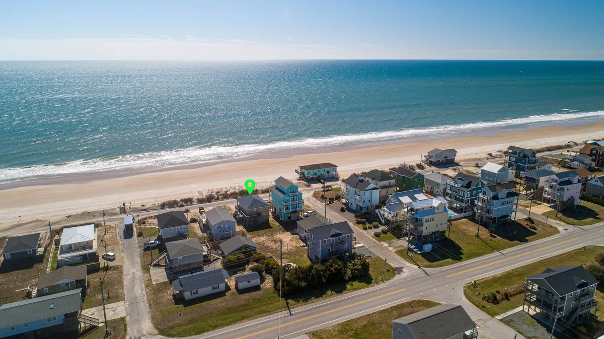 A scenic coastal vista featuring ocean waves, beachfront homes, and a sandy road leading directly to the beach. The composition highlights the immediate access to the beach and the sense of quiet privacy, capturing the essence of romantic walks and seaside exploration.