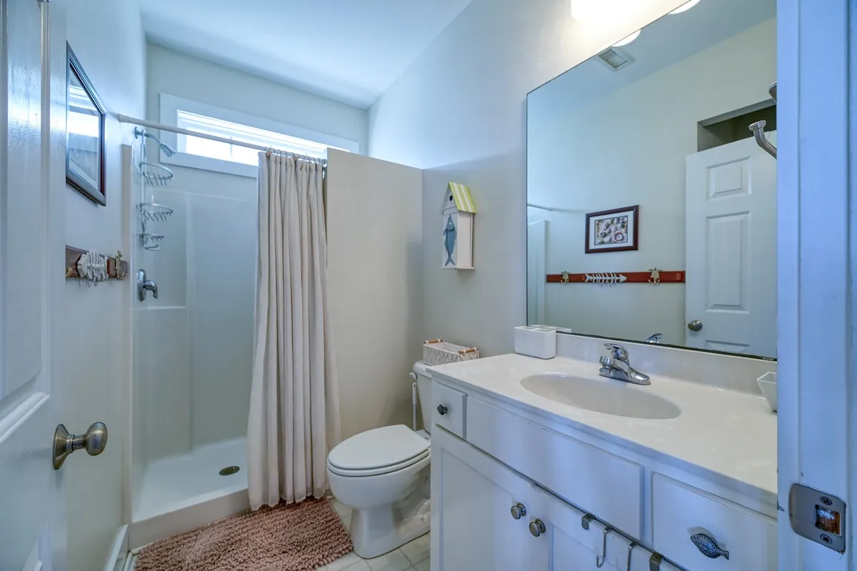 This serene bathroom features a vanity with mirror, a step-in shower area, and a toilet. The inviting and clean atmosphere offers a glimpse of the modern amenities available for relaxation after a day at the beach.
