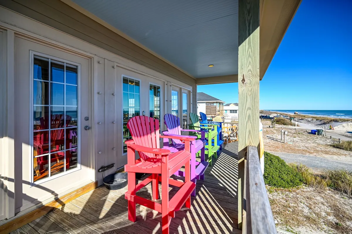 A vibrant outdoor deck lined with cheerful Adirondack chairs, all positioned to face a panoramic ocean view. The spacious deck invites couples to unwind together, whether for sunrise coffees, sunset cocktails, or stargazing under the evening sky.