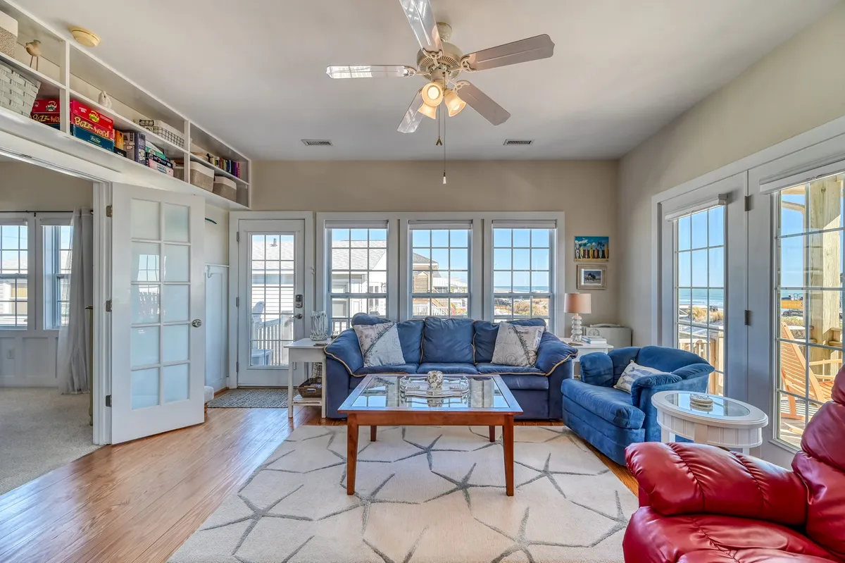A bright living space with large windows offering expansive views, a plush blue sectional sofa, and a wooden coffee table. The room radiates comfort, perfect for relaxing, reading, or entertaining with the backdrop of sunlit scenery.