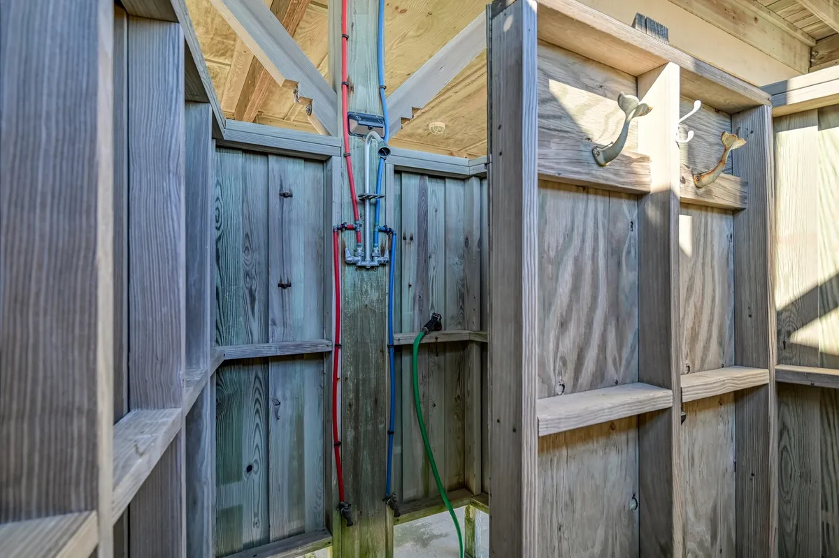 A cozy, wood-paneled interior space shows shower fixtures and functional hooks for beach gear, suggesting a convenient spot for rinsing off and managing sandy belongings right as you arrive home.